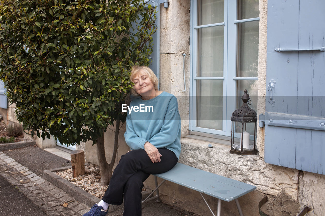 Elderly lady relaxing by her home with greenery and blue shutters