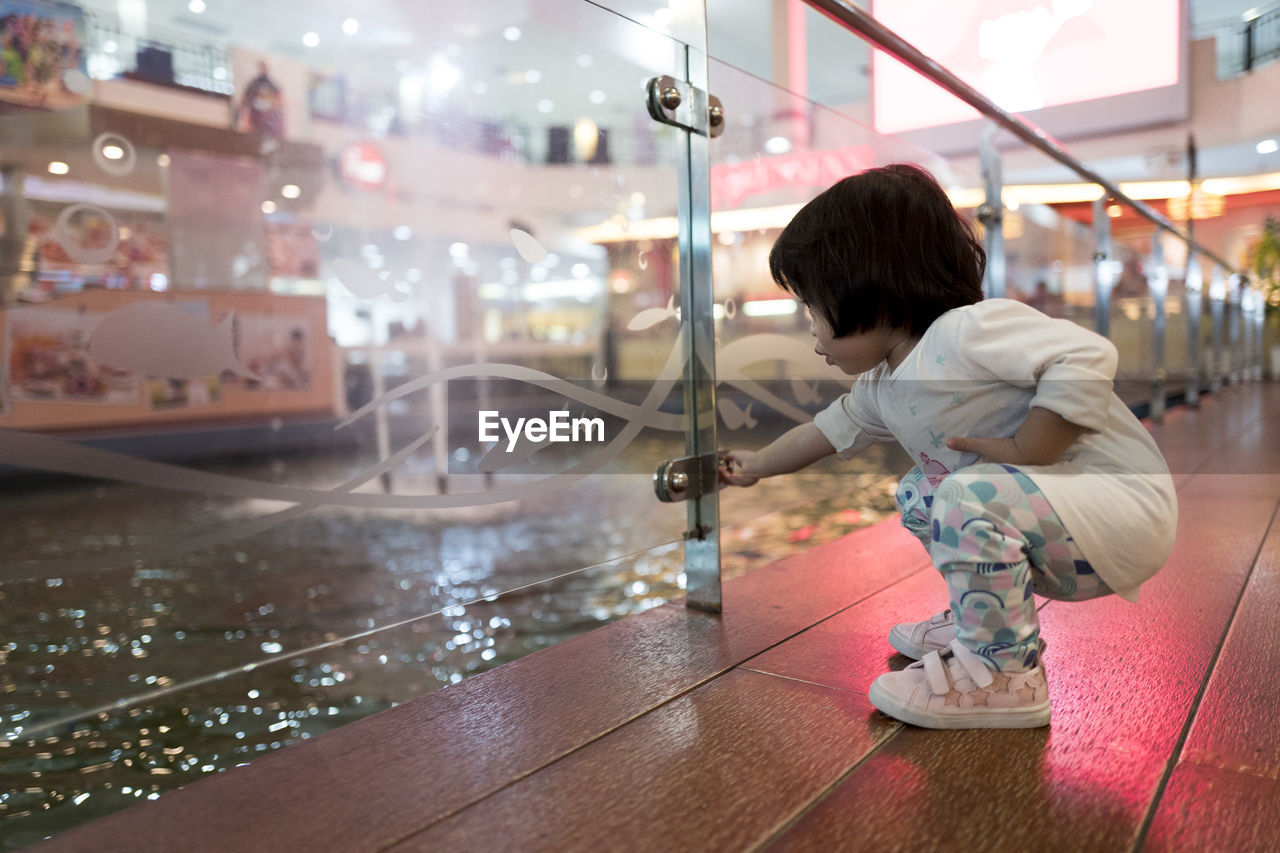 Girl holding glass knob while crouching in shopping mall