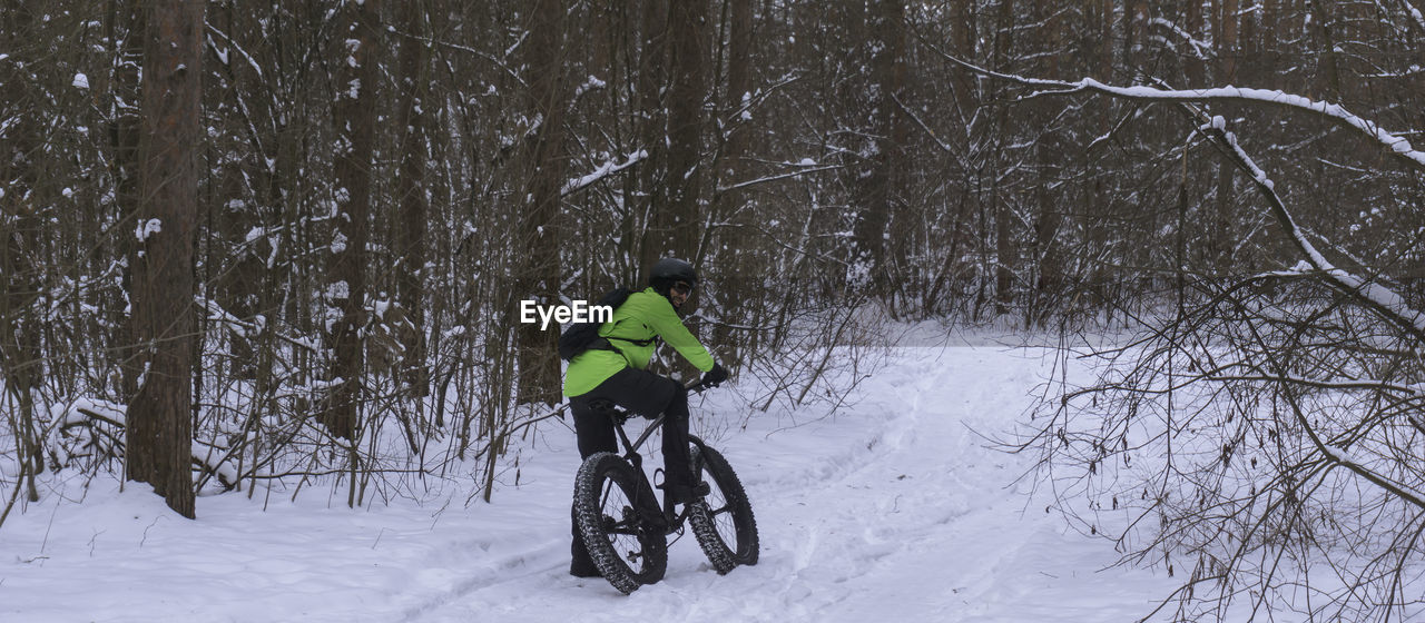 Rear view of man cycling on snow covered land