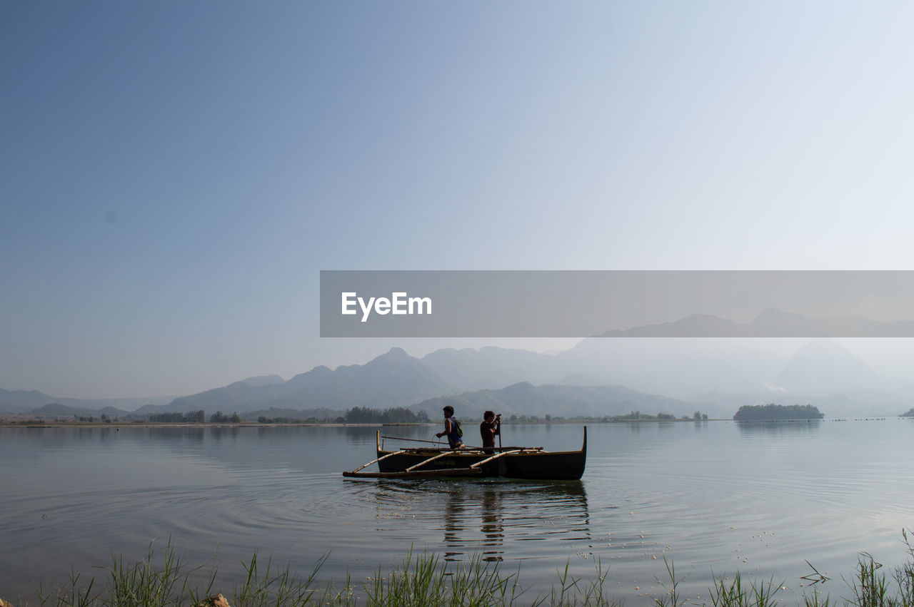 Men and boat in sea against clear sky