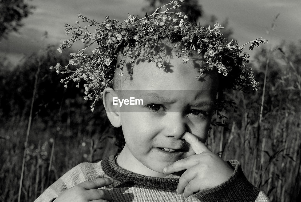 Portrait of boy wearing flower wreath while picking nose on field