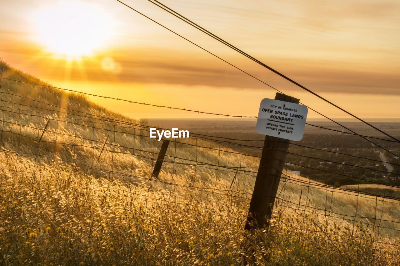 Barbed wire fence on field against sky during sunrise