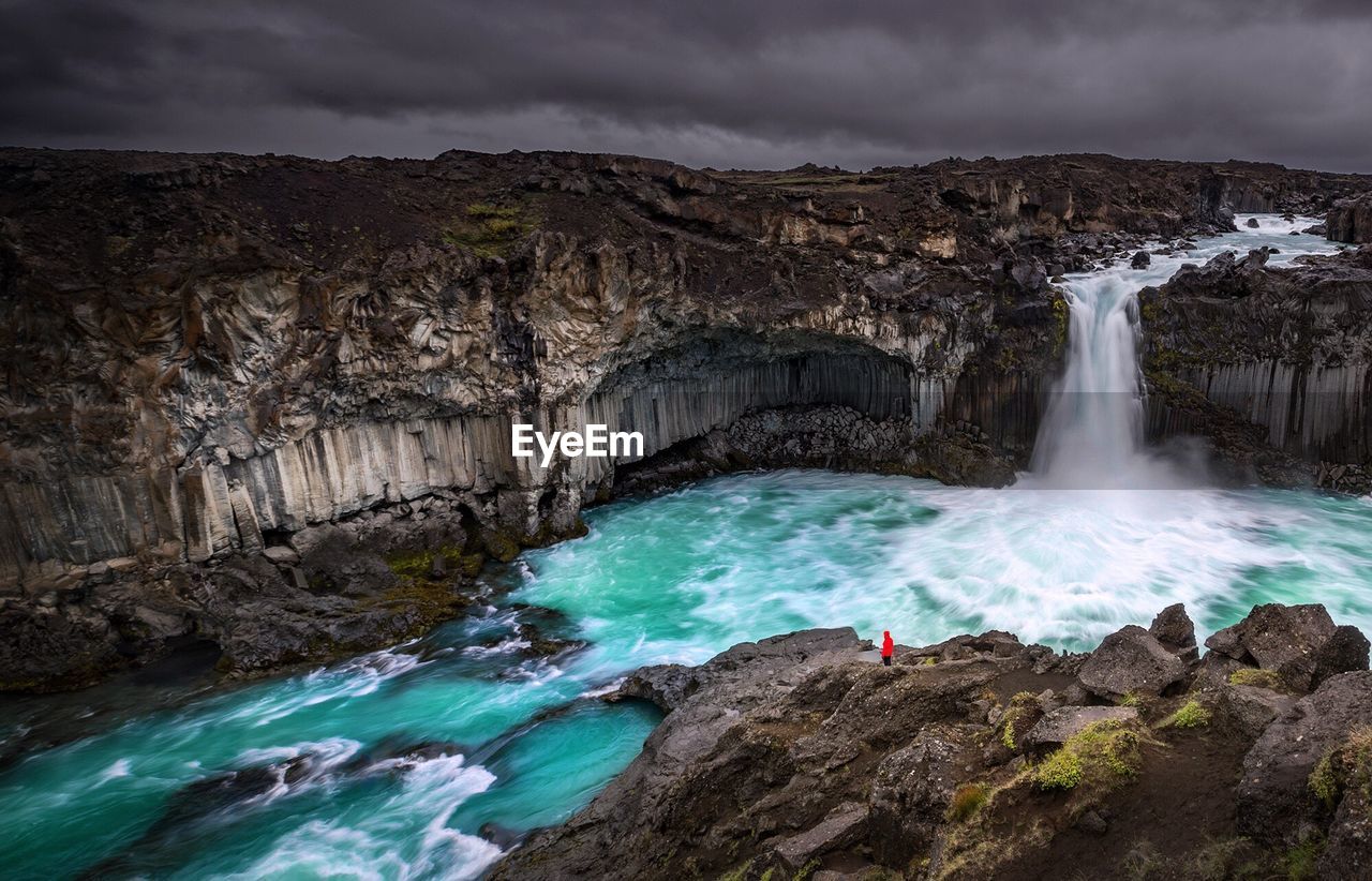 Scenic view of waterfall against stormy clouds