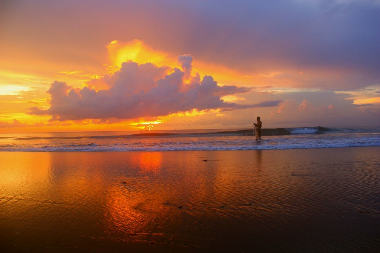 Person standing in sea against sky during sunset