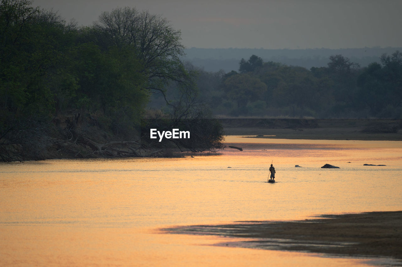 Person sailing on boat over river during sunset