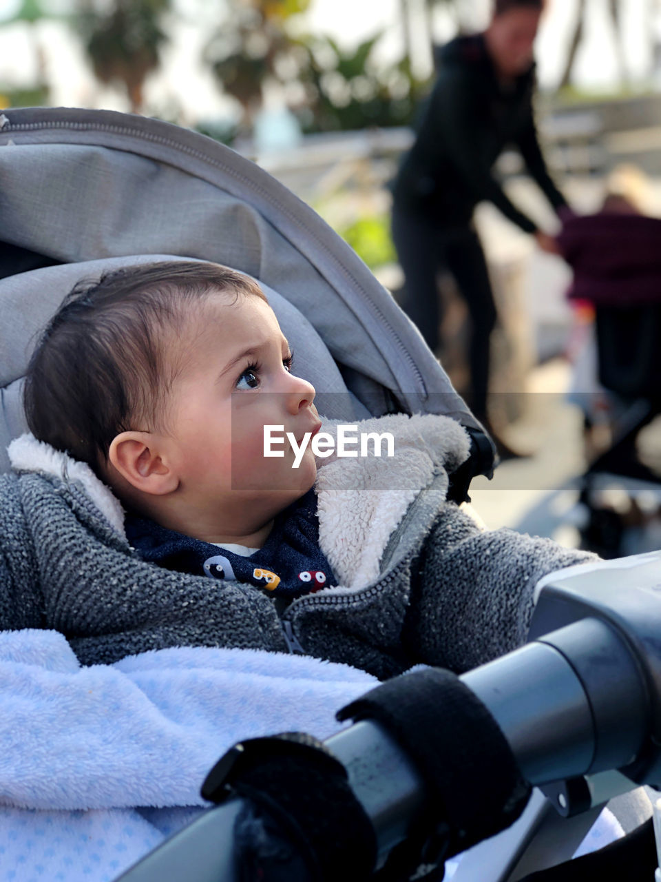 Little boy in his baby carriage, looking around, serious on a winter day. with a blanket on her lap.