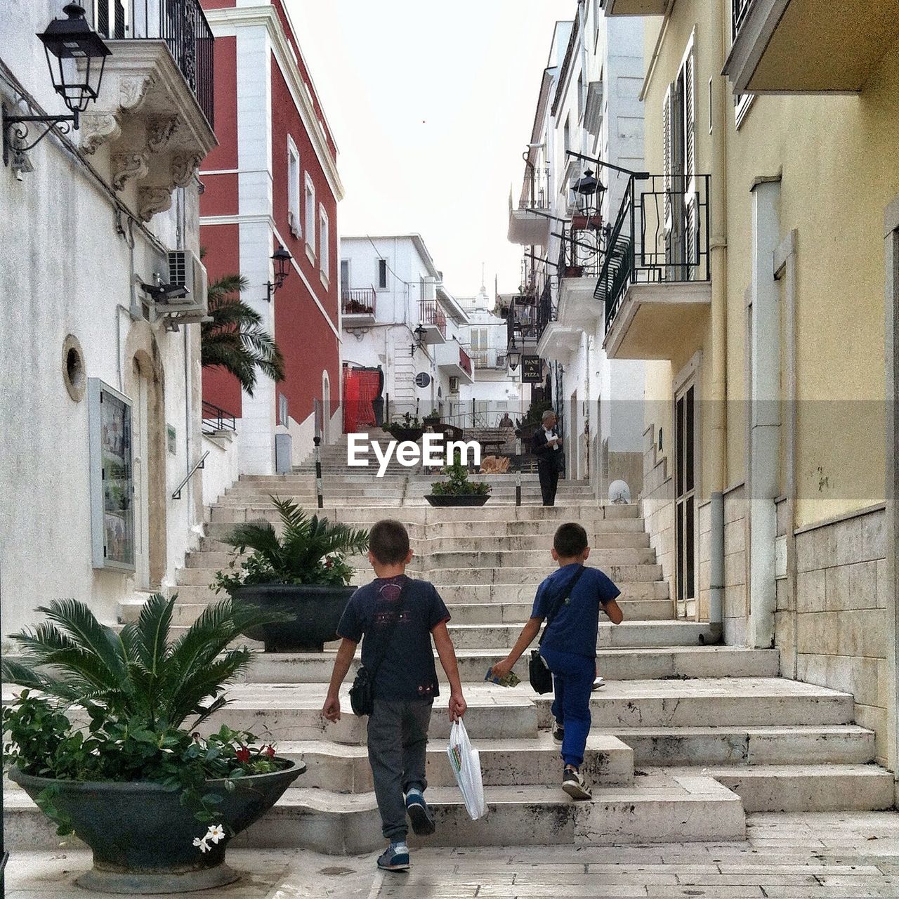 REAR VIEW OF PEOPLE WALKING ON COBBLESTONE STREET