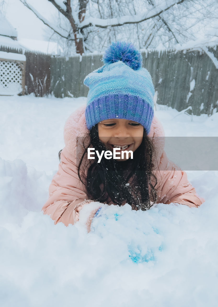 Diverse mixed race pre school toddler girl outdoors in winter playing with snow 