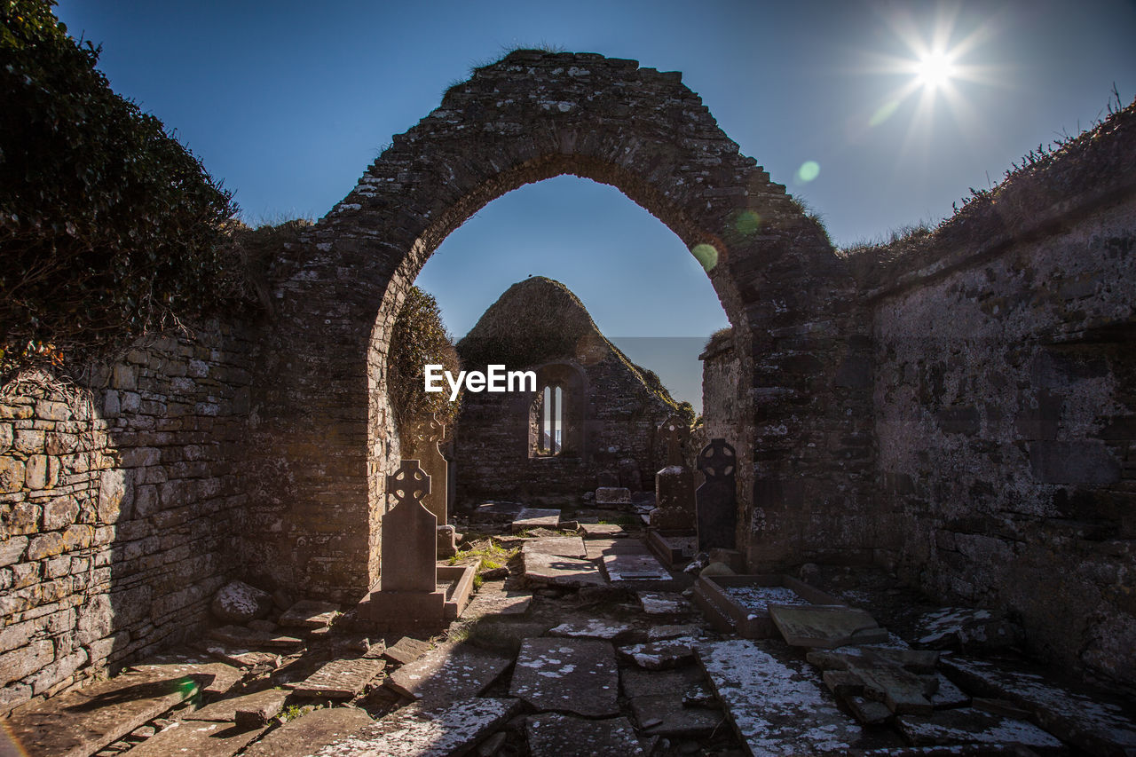 Archway in abandoned cemetery against sky on sunny day