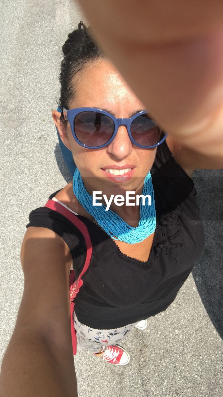 High angle view portrait of woman wearing sunglasses standing on road