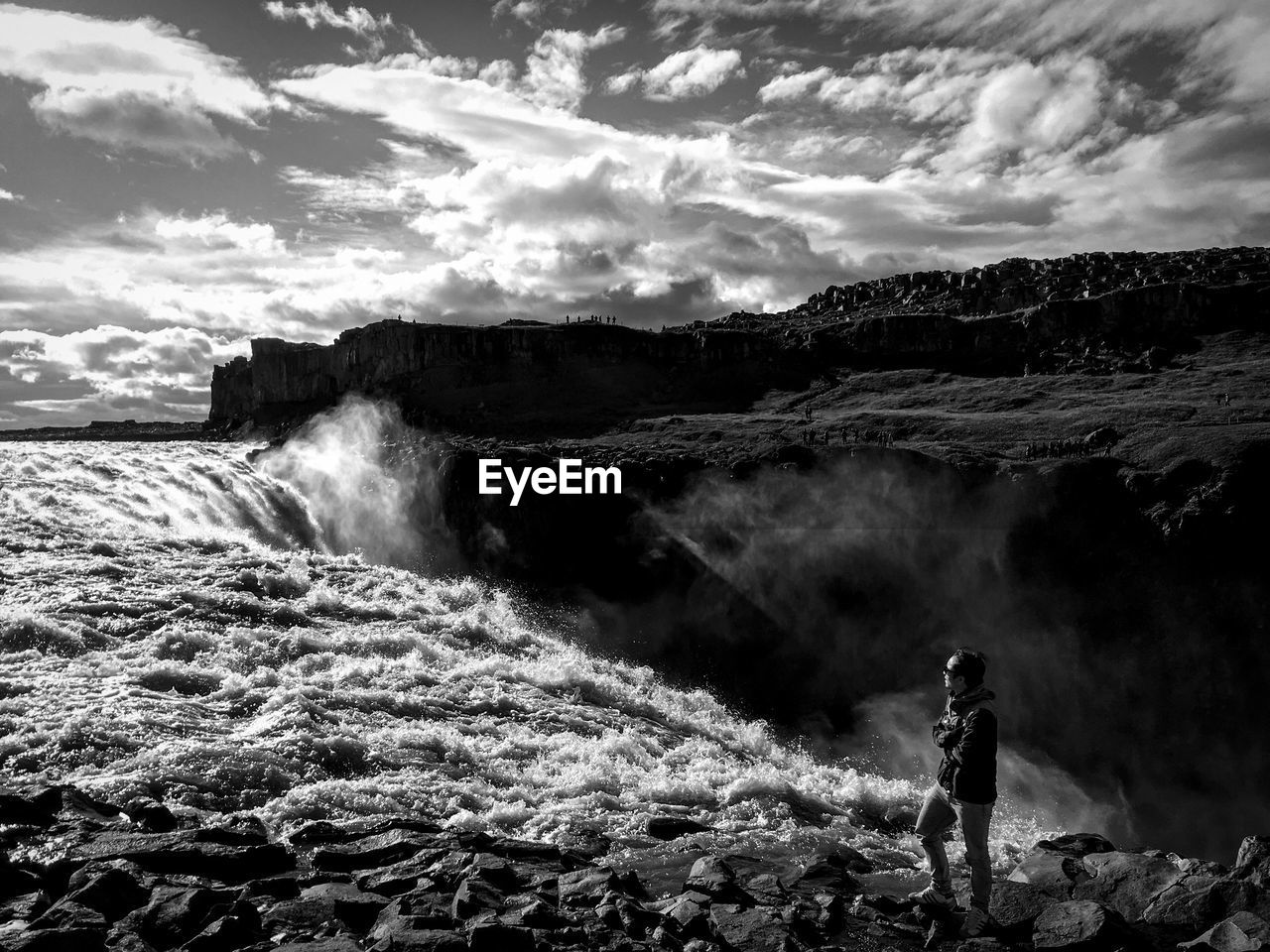Man standing by dettifoss against cloudy sky