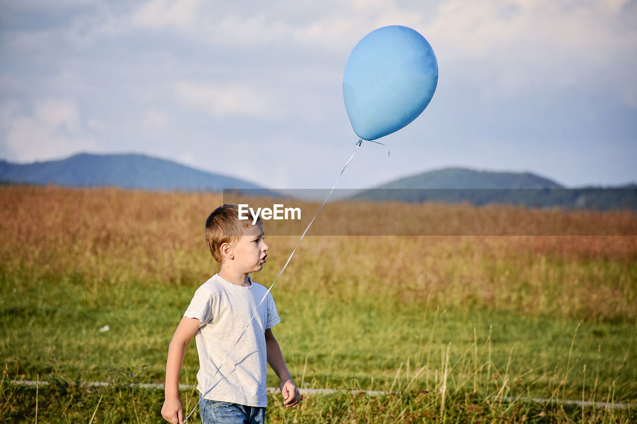 FULL LENGTH OF A BOY HOLDING BALLOONS ON FIELD