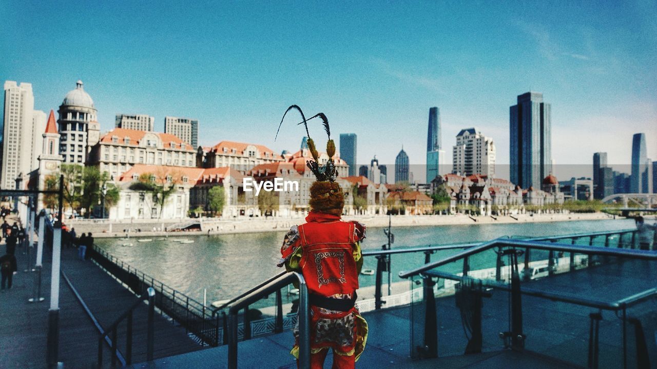 Person standing by railing against buildings in city against sky