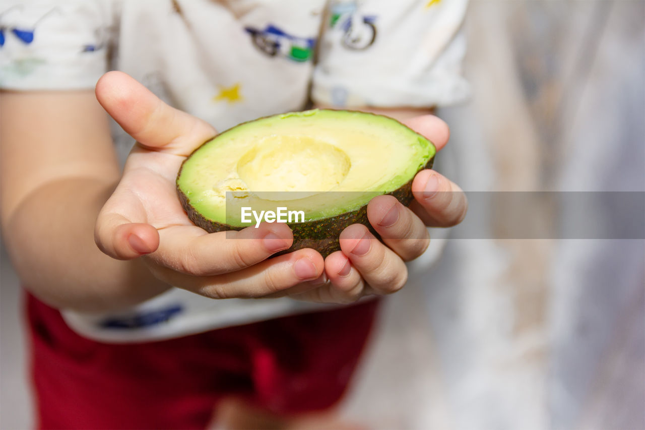 A child holds a cut avocado in his hands close-up