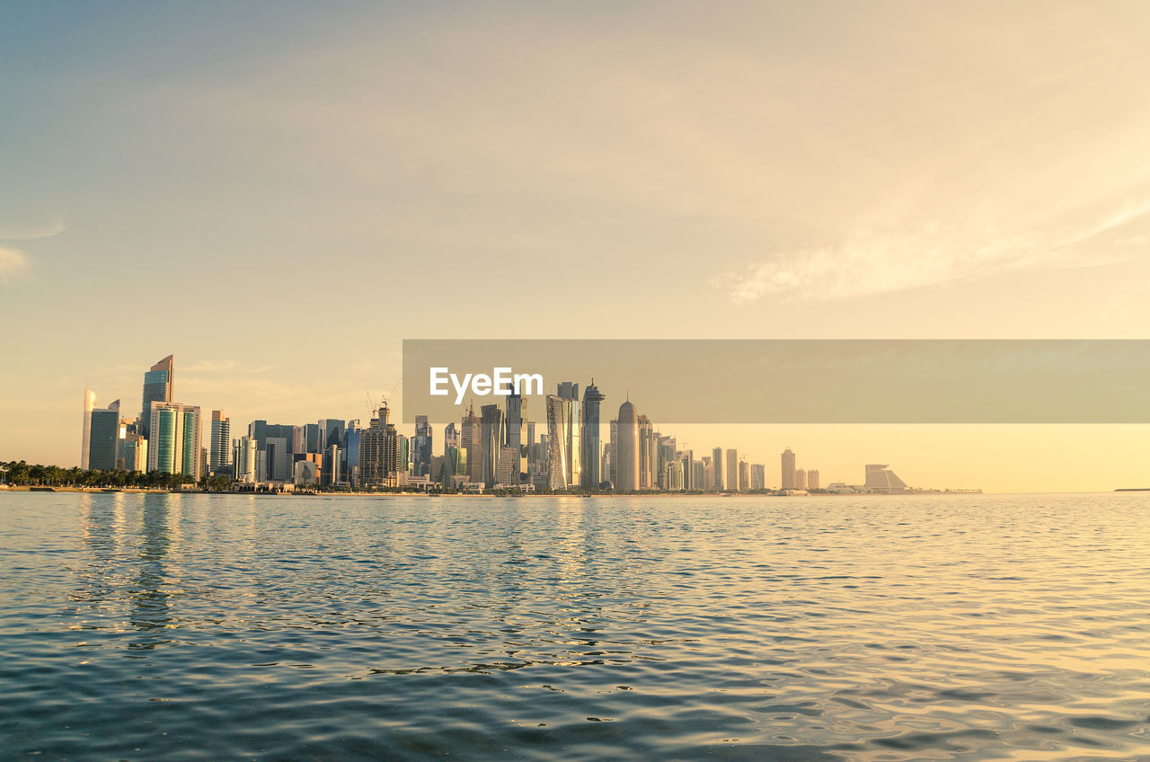 Sea and buildings against sky during sunset