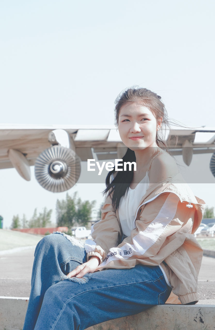 Portrait of smiling young woman sitting against sky