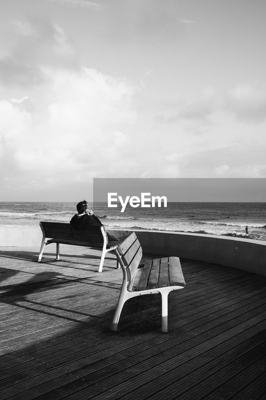 Man sitting on bench looking at sea against sky
