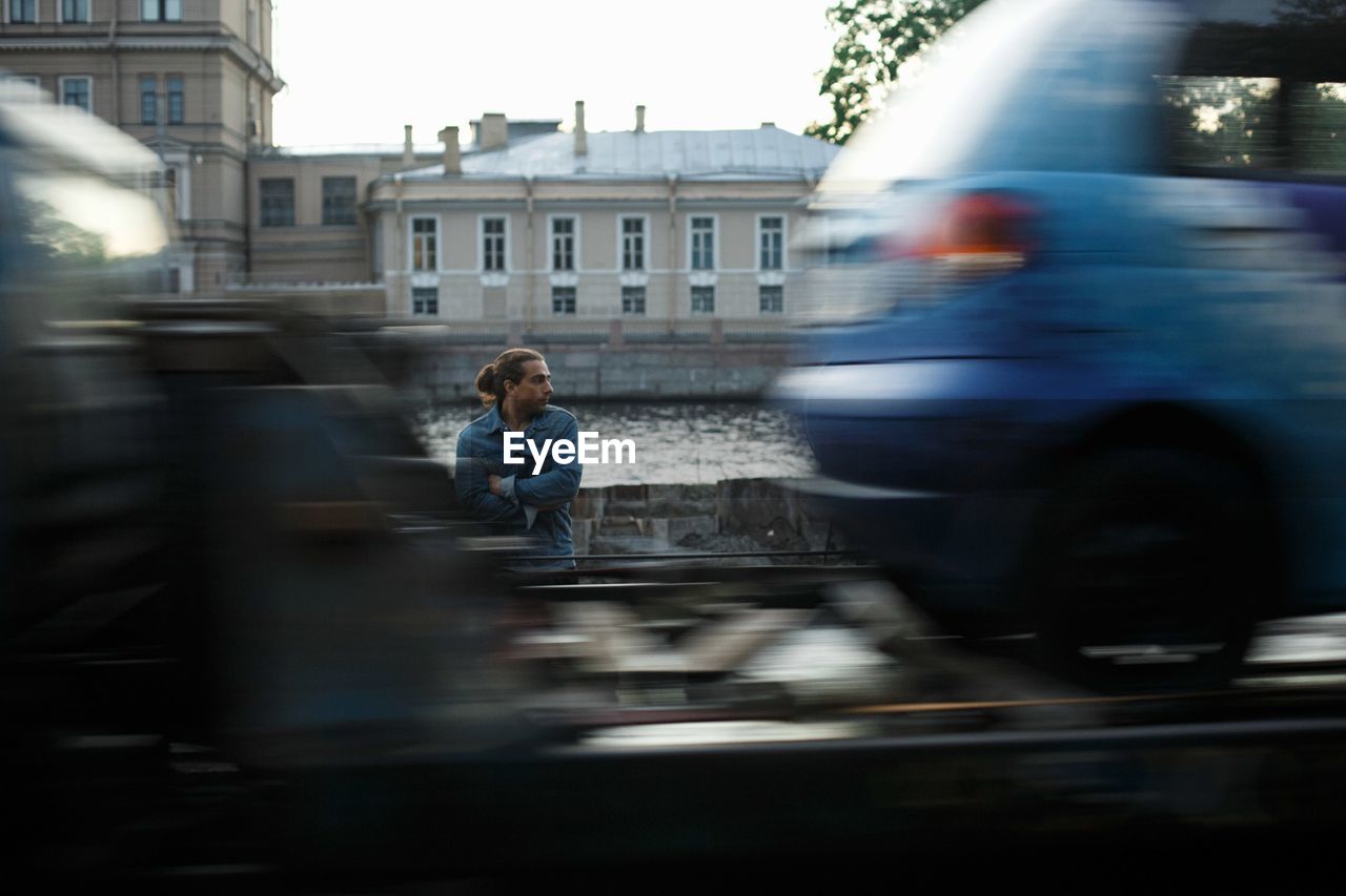 Blurred motion of vehicles against man standing by river