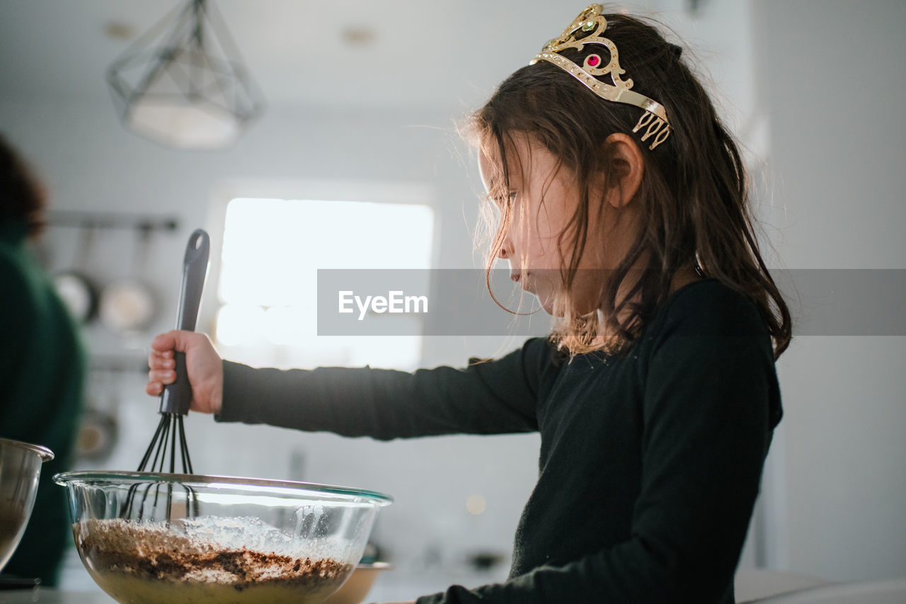 Preschool age girl in tiara baking with mixing bowl and whisk