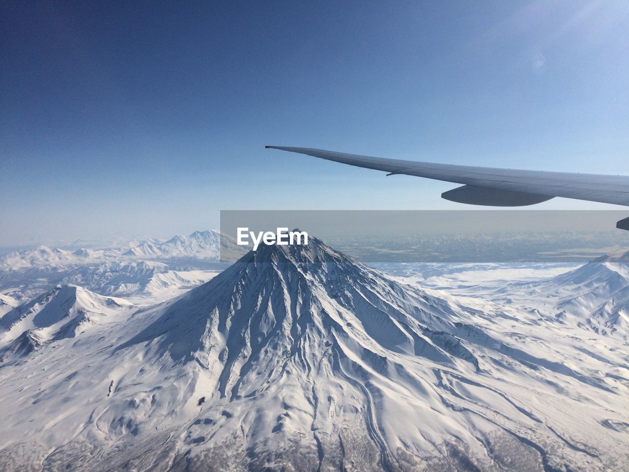 Cropped image of aircraft wing over snow covered mountains against sky