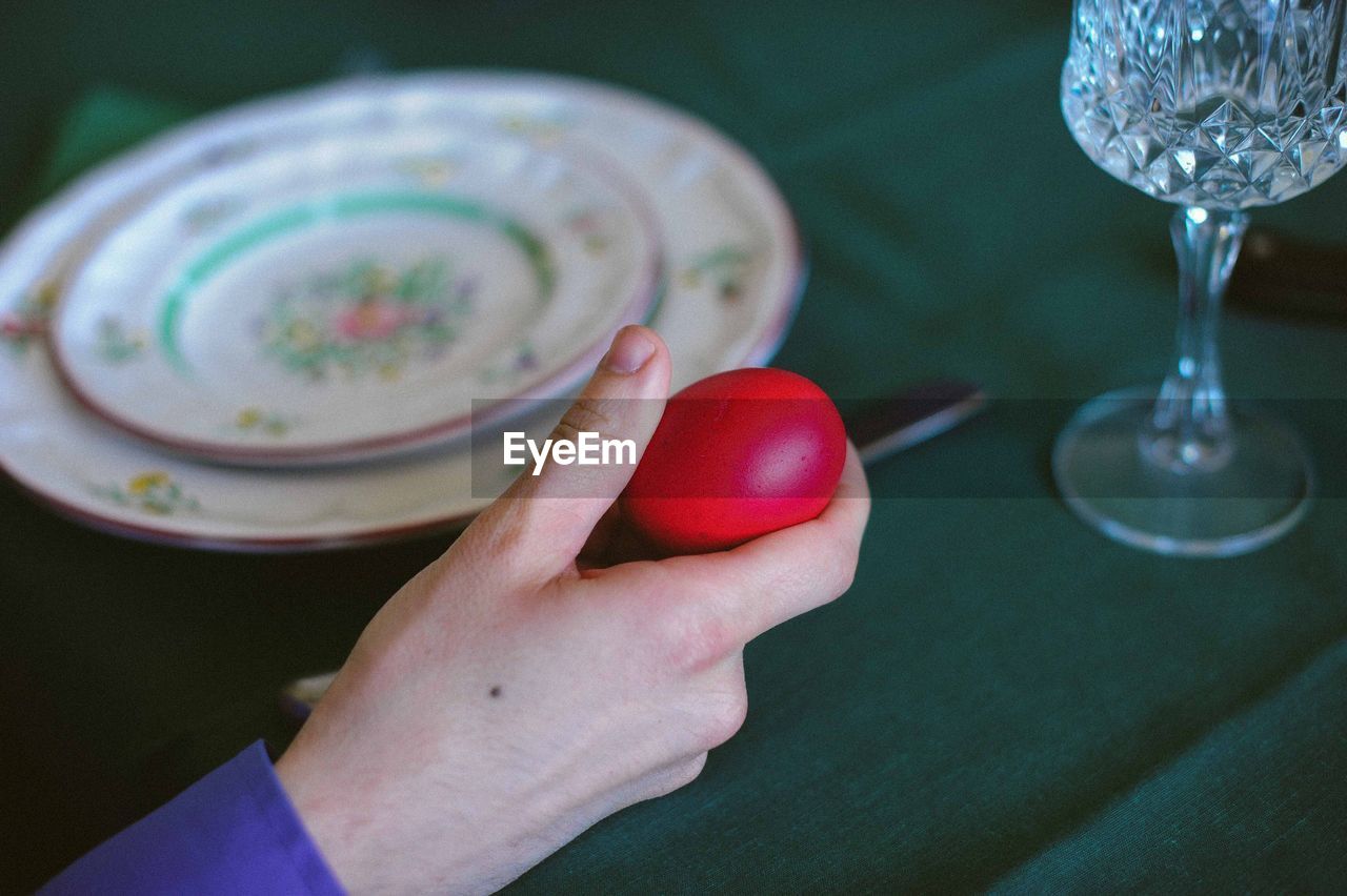 Cropped image of person holding red easter egg at table