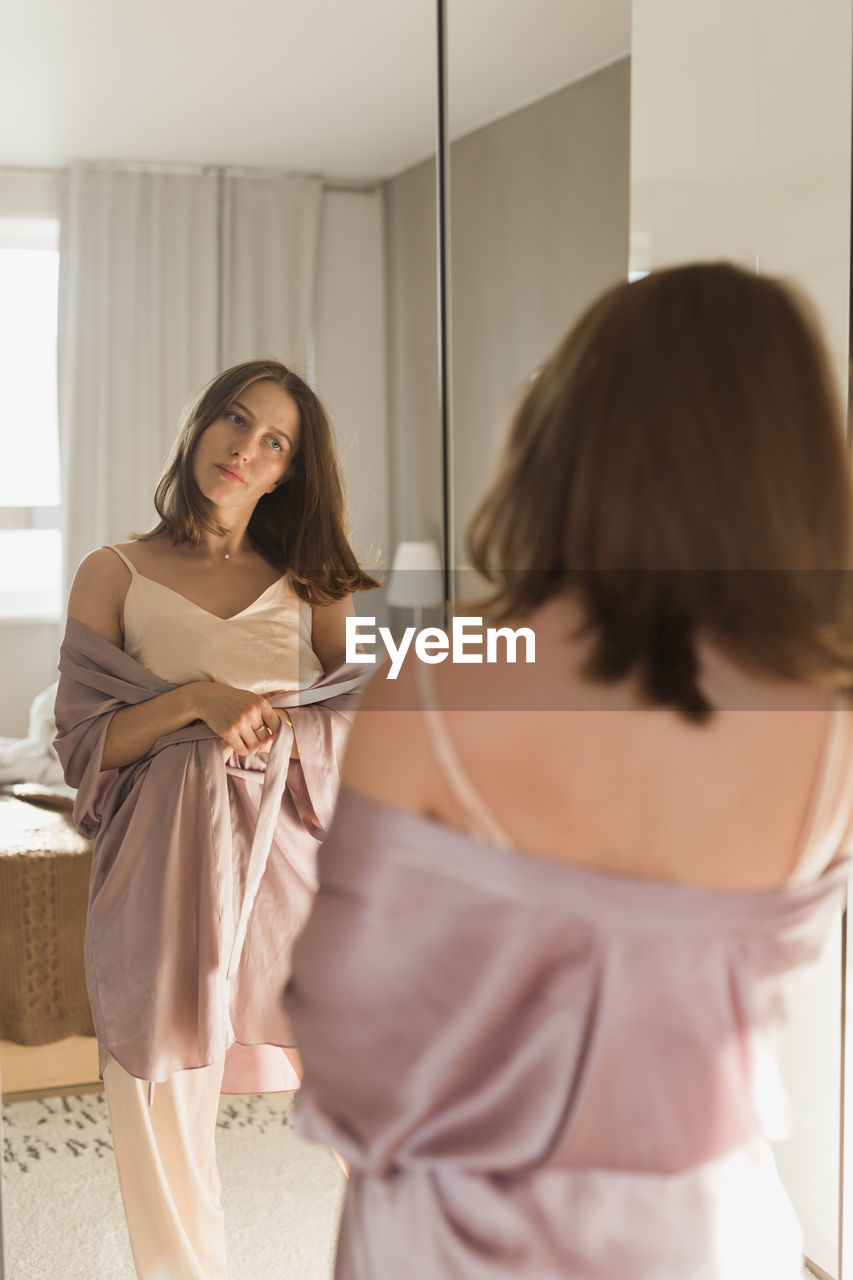 Rear view of young woman standing by mirror