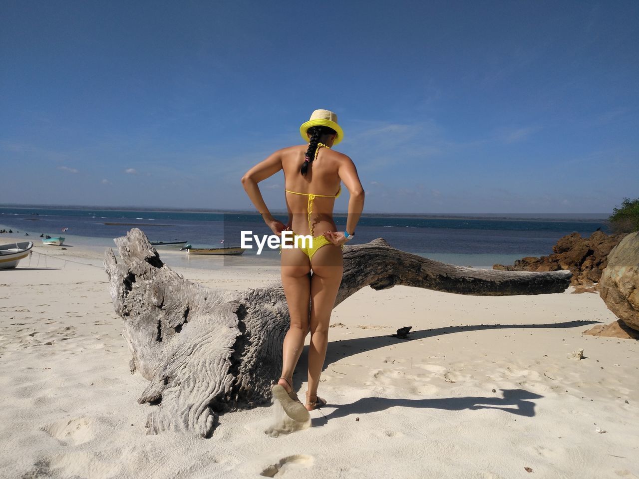 Rear view of mid adult woman in yellow bikini walking at beach against blue sky during sunny day