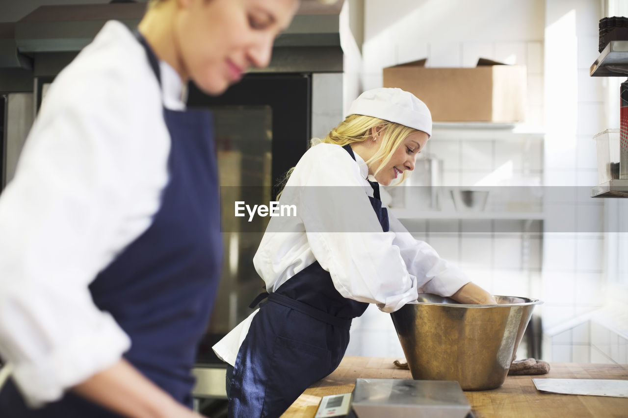 Young female baker working with colleague in commercial kitchen