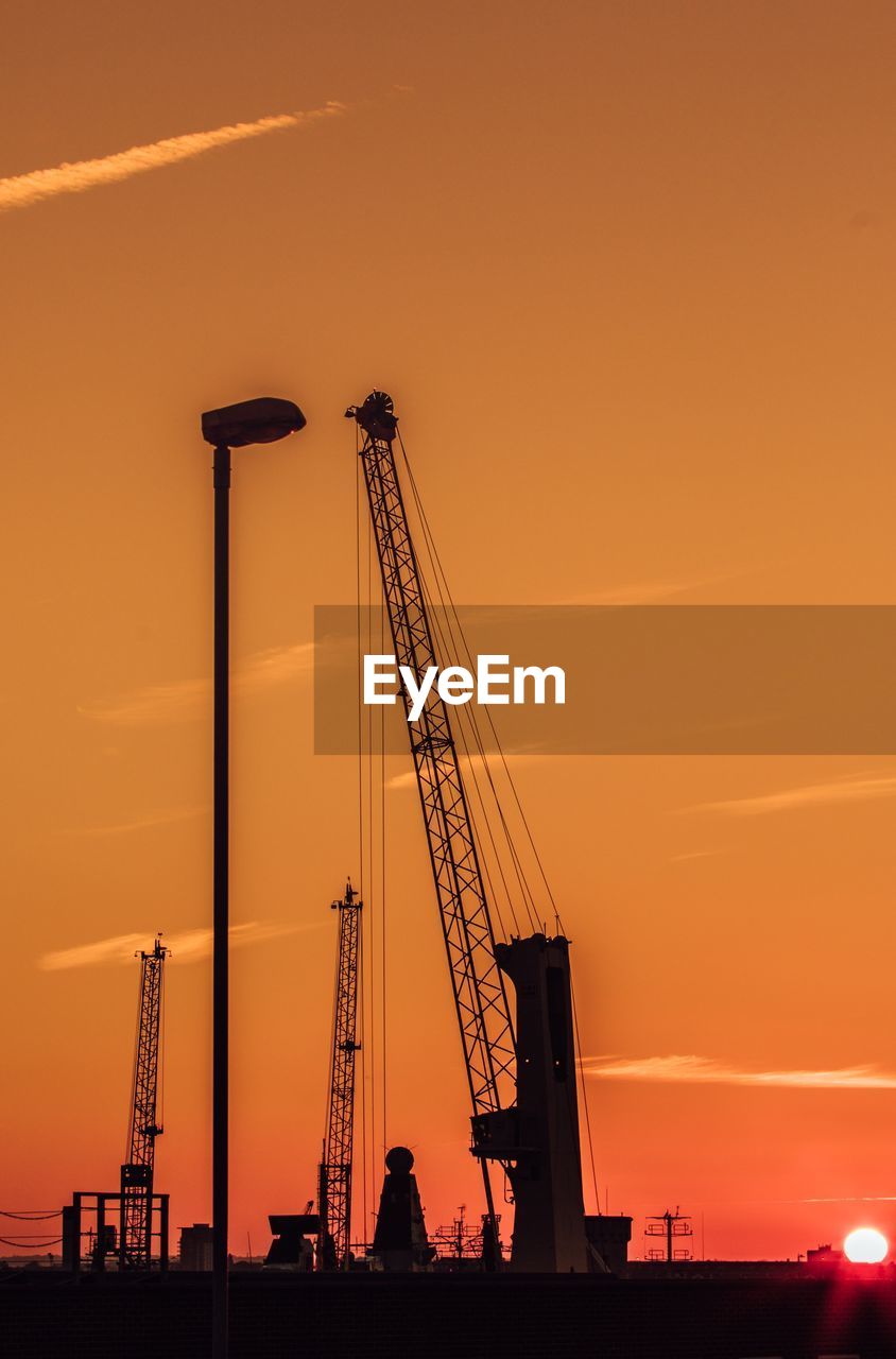 Low angle view of silhouette cranes against sky at sunset