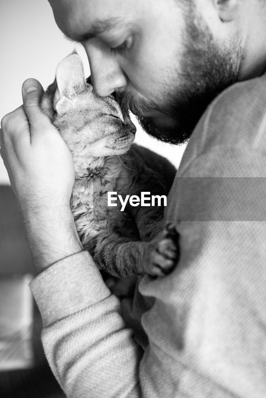 Black and white photo. close-up of beard man is holding his cute purring devon rex cat. 