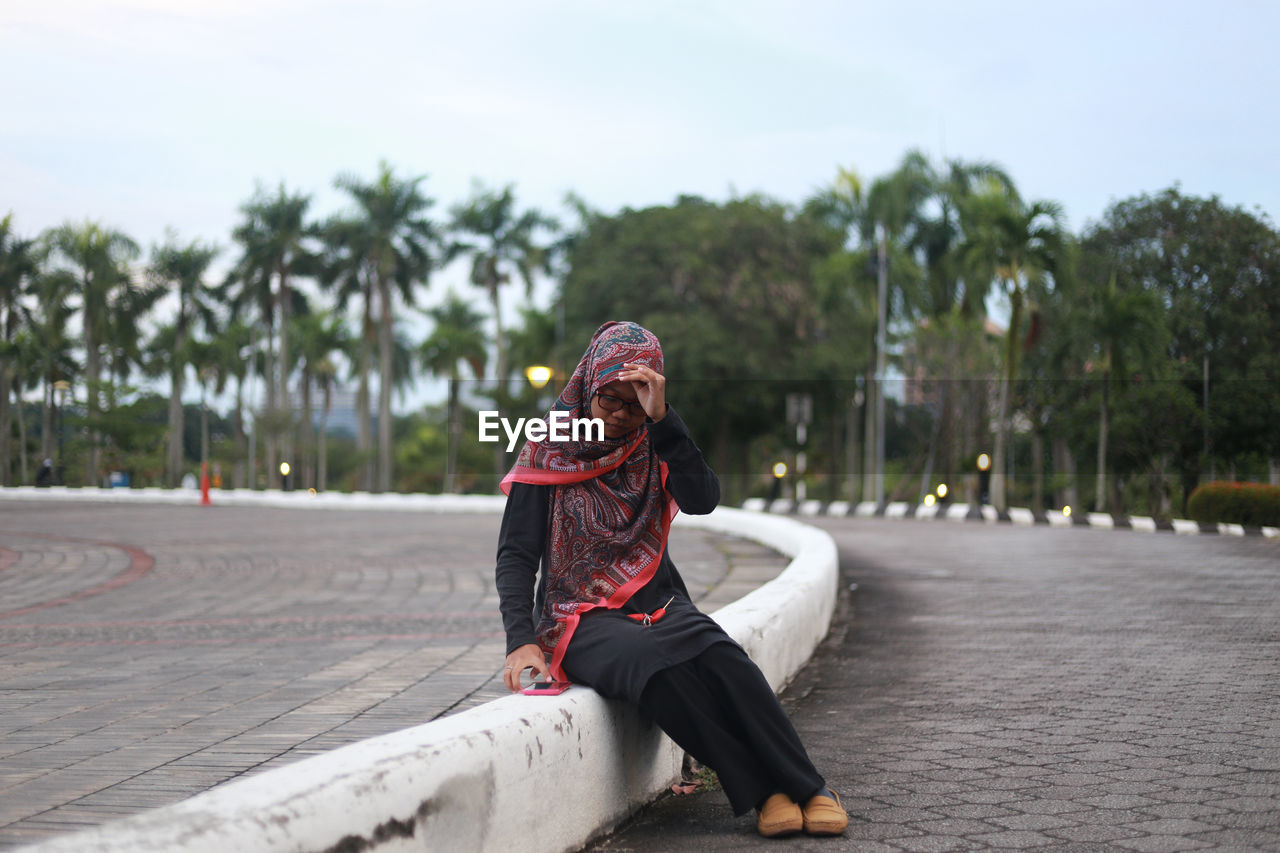 Thoughtful young woman sitting on dividing line at street