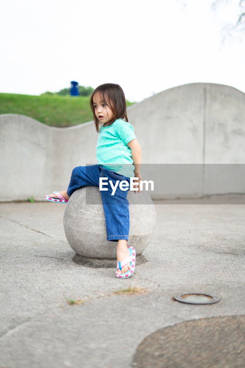 Full length of girl sitting on rock against clear sky