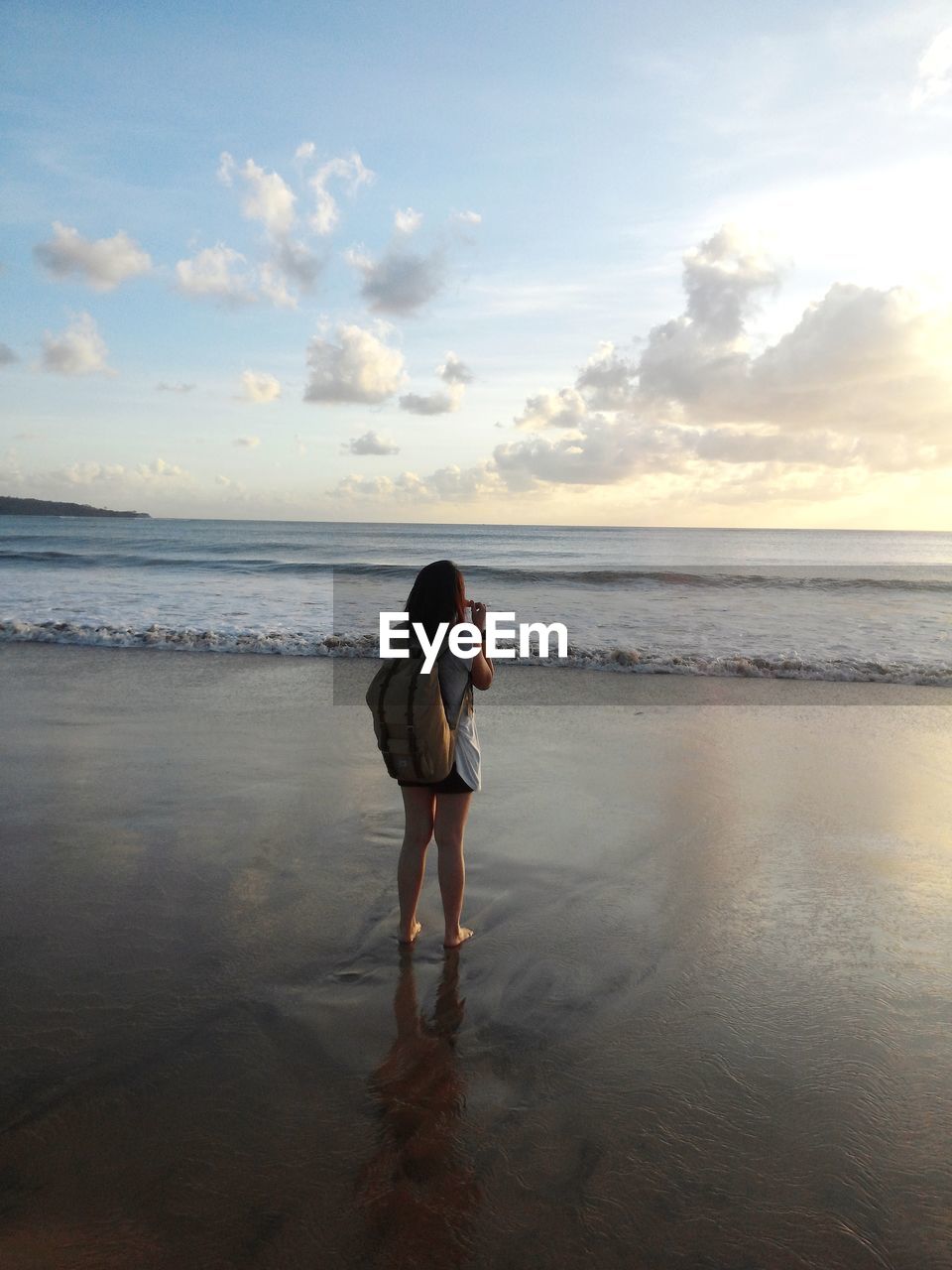 Rear view of woman standing at beach during sunset