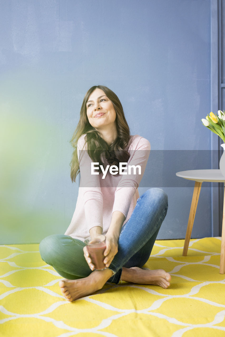 Smiling woman sitting on floor holding glass of juice