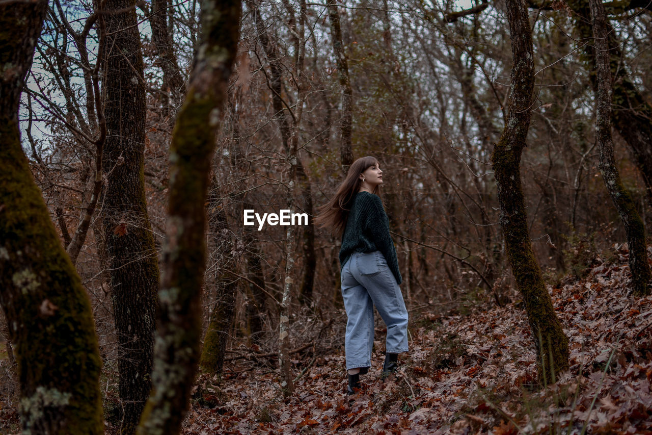 FULL LENGTH OF WOMAN STANDING ON TREE TRUNK