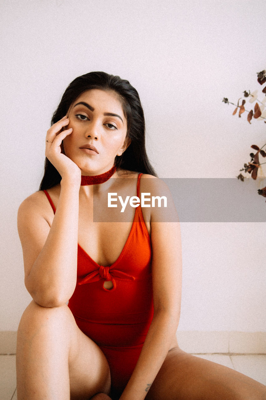 Portrait of young woman sitting against wall at home