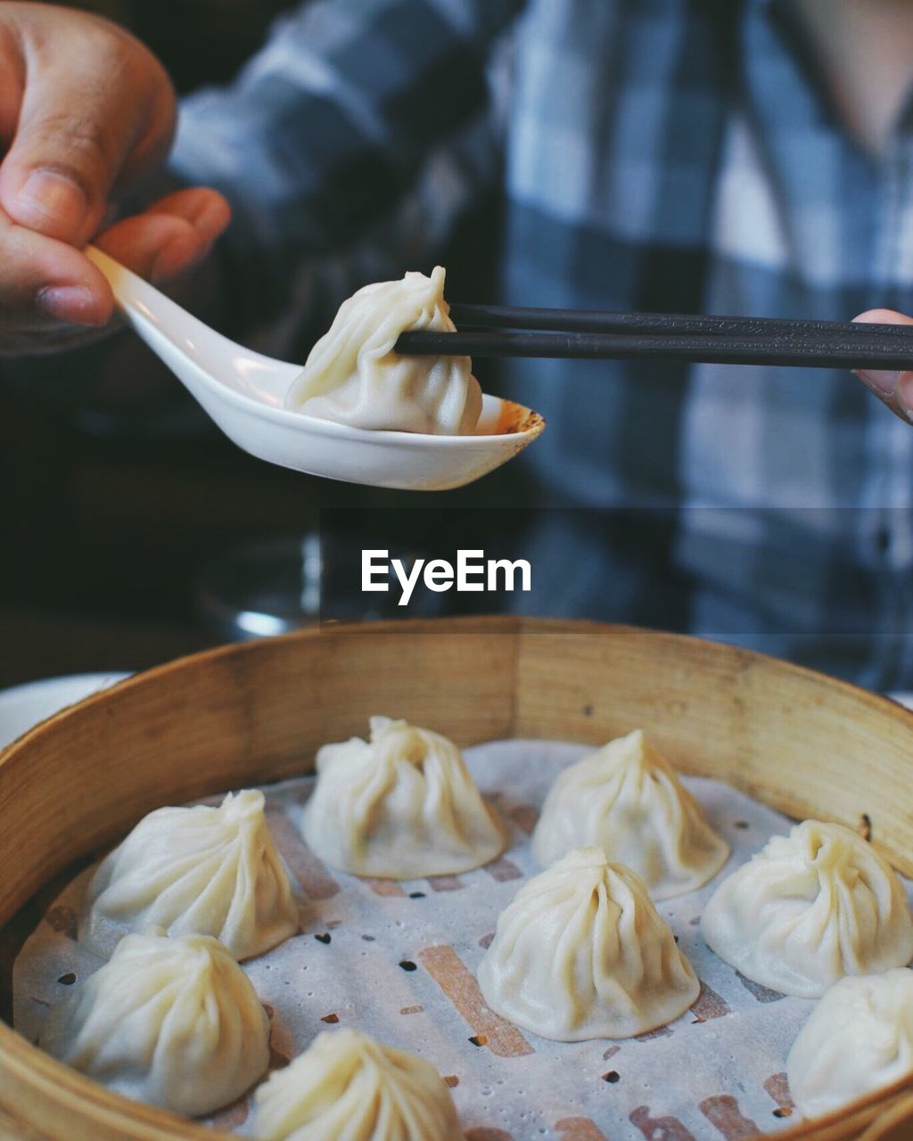Cropped image of person holding dumpling with chopsticks in spoon