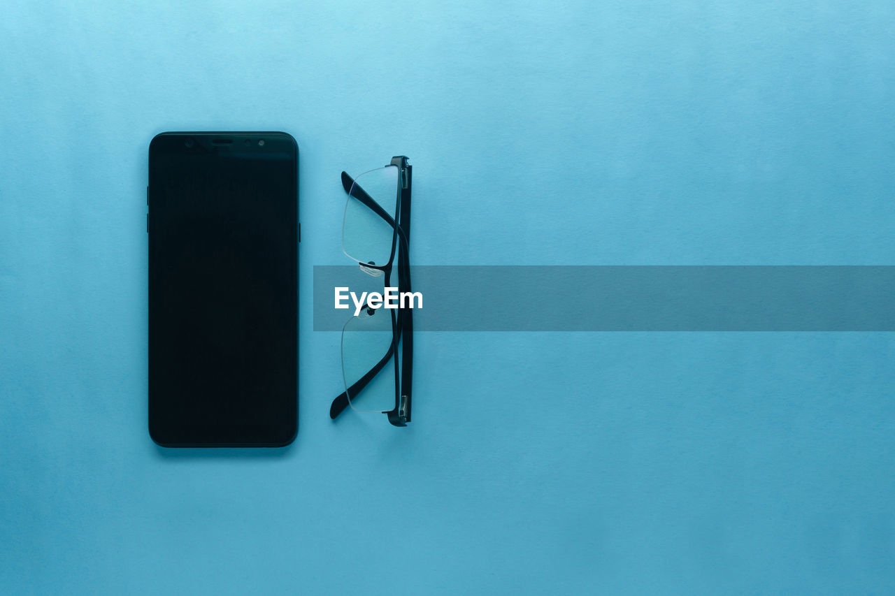 High angle view of the gadget and glasses on table against blue background