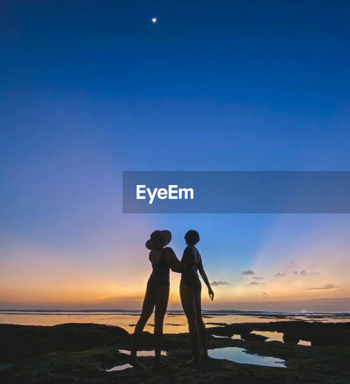 Rear view of man standing on beach against sky during sunset