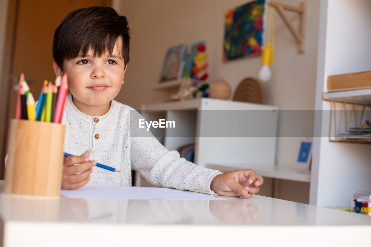 Cute boy holding colored pencil at home