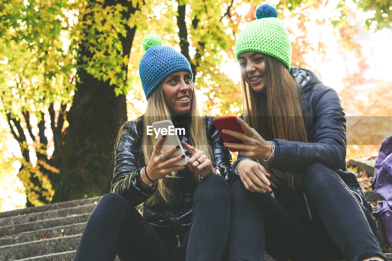 Two girls sitting in the park using smartphone. teen using mobile phone. sisters chat with friends.