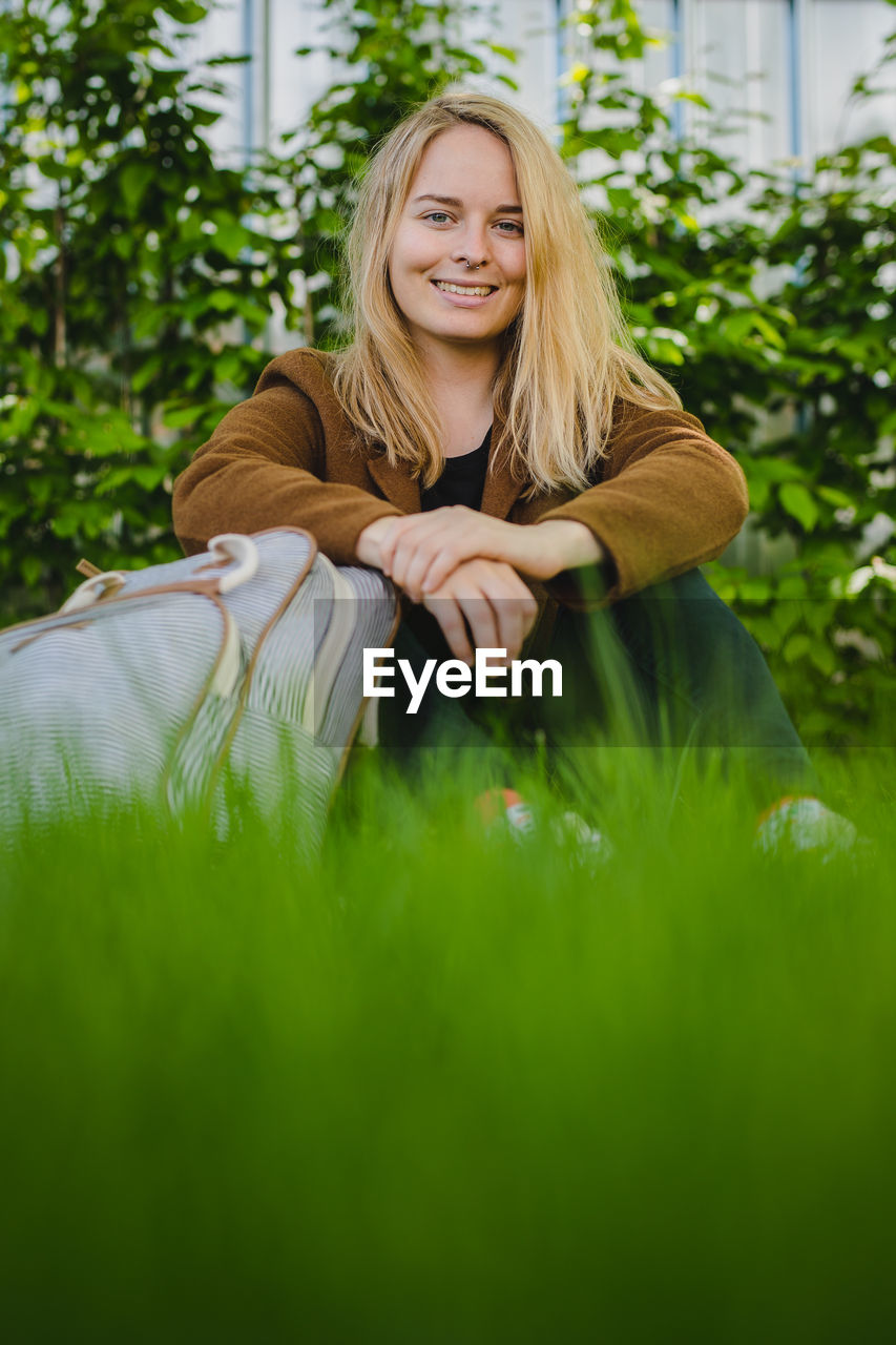 Portrait of smiling young woman with blond hair sitting on grass