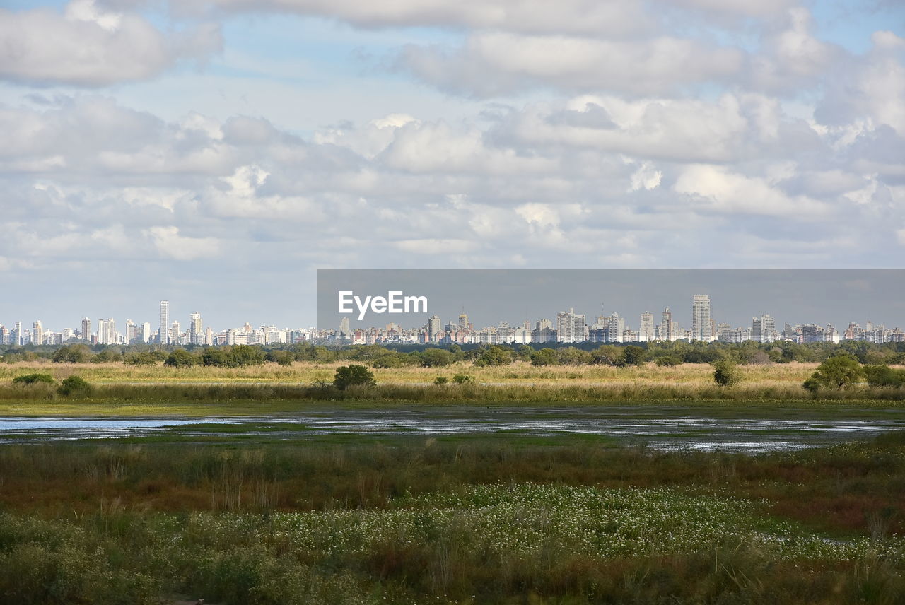 Scenic view of field and cityscape against sky