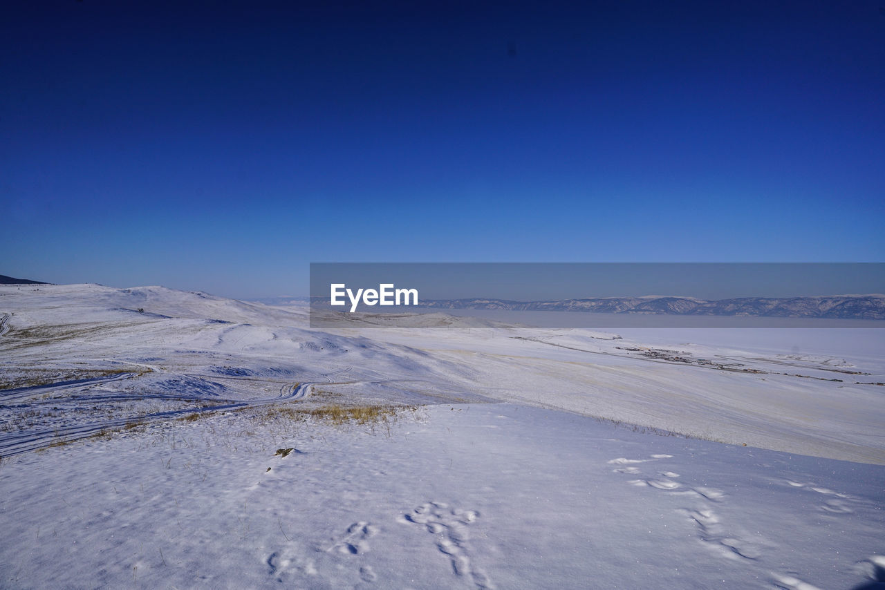 Scenic view of snow covered land against clear blue sky