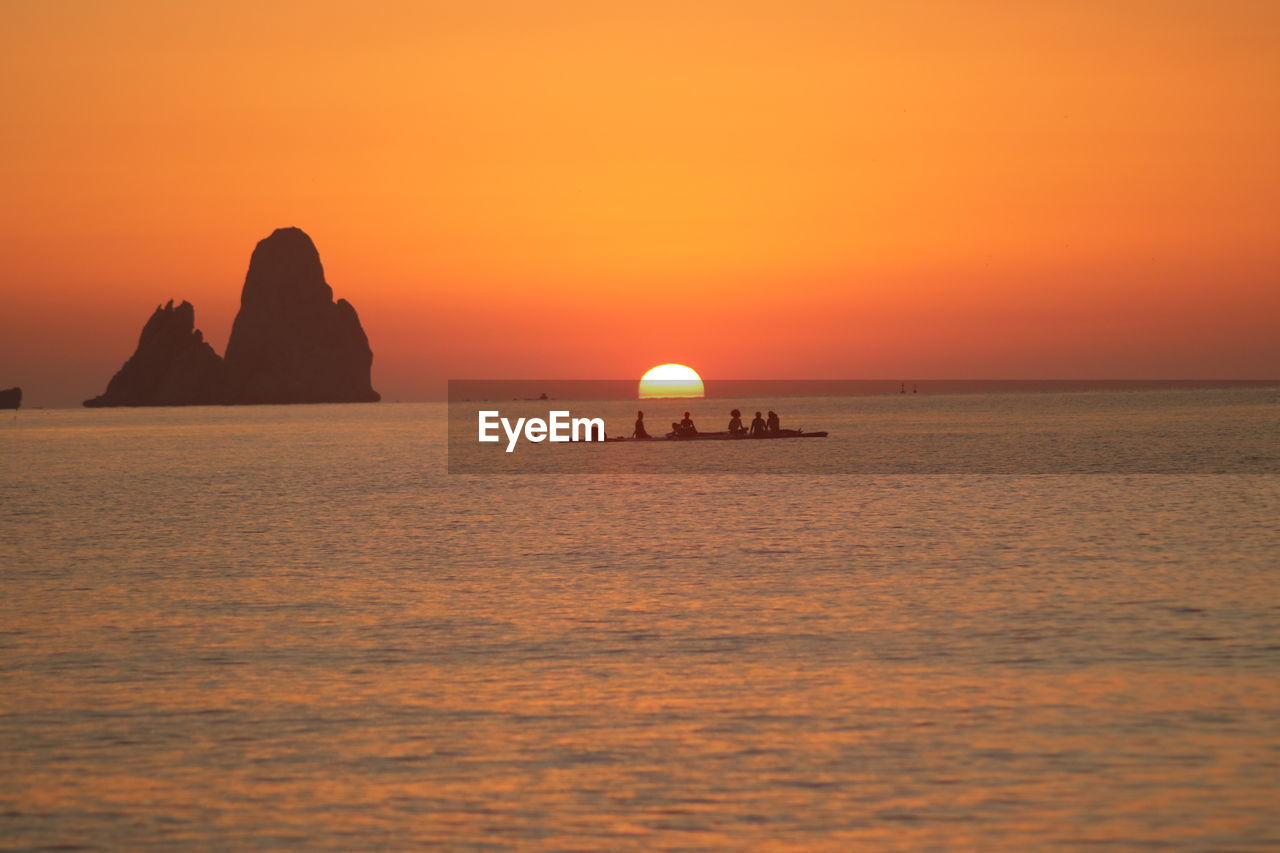 SILHOUETTE ROCK IN SEA AGAINST ORANGE SKY