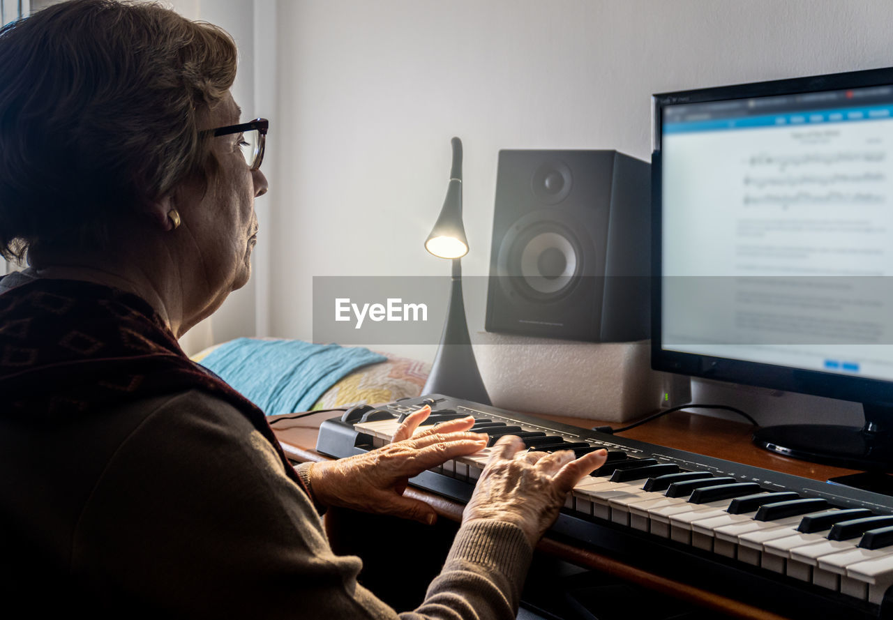 Caucasian elderly woman learning music and playing the musical keyboard.