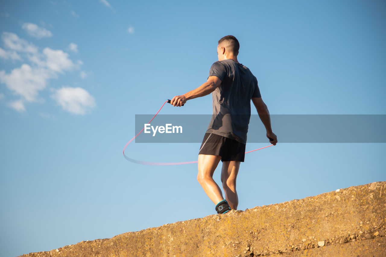 Low angle view of man exercising against blue sky