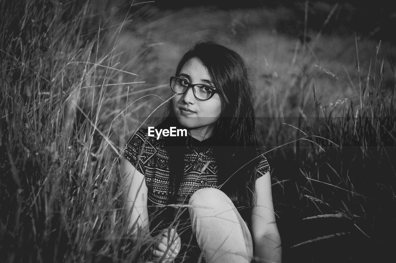 Young woman sitting amidst grass on field