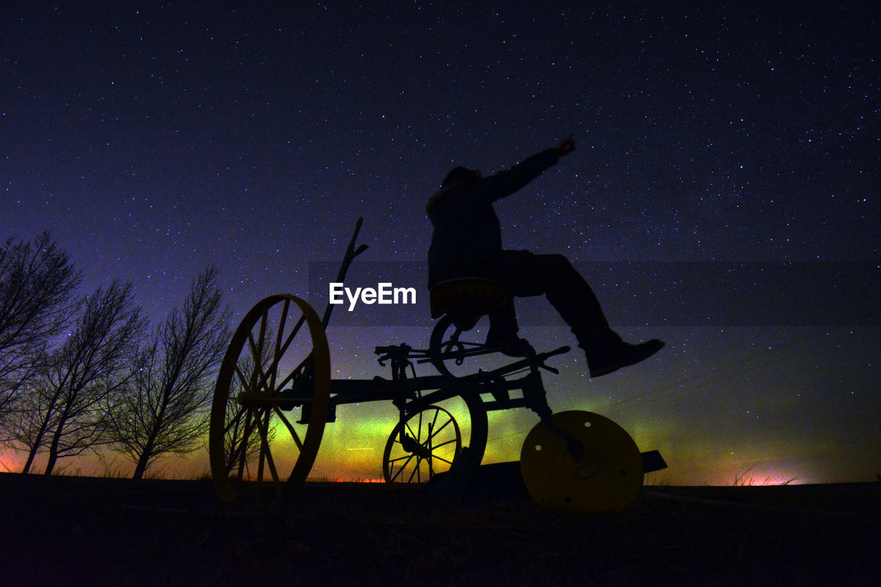 low angle view of silhouette man riding bicycle against sky at night