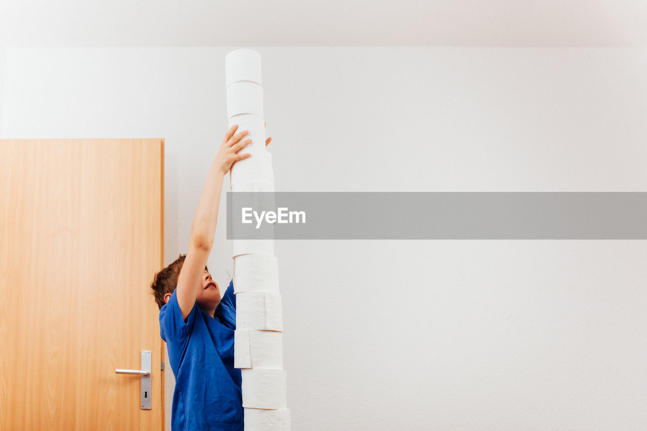 Boy stacking tissue rolls against wall